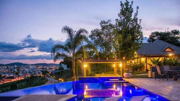 Piscina com vista para a paisagem urbana ao entardecer, área de estar coberta e um terraço com mobiliário de exterior.