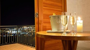 Varanda com vista para luzes da cidade, porta de madeira, balde de metal e duas taças de champanhe.