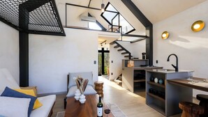 Een modern interieur met een houten eettafel, een bank met kussens, een keuken en een trap naar een hoger niveau.