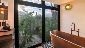 Een moderne badkamer met een groot raam, een koperen badkuip en een houten wastafelmeubel.
