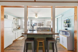 A kitchen with a central island, wooden stools, and a view of the backyard through large windows. - Lakefront Cottage #3 | Dock | Mtn & Lake Views (Bristol)