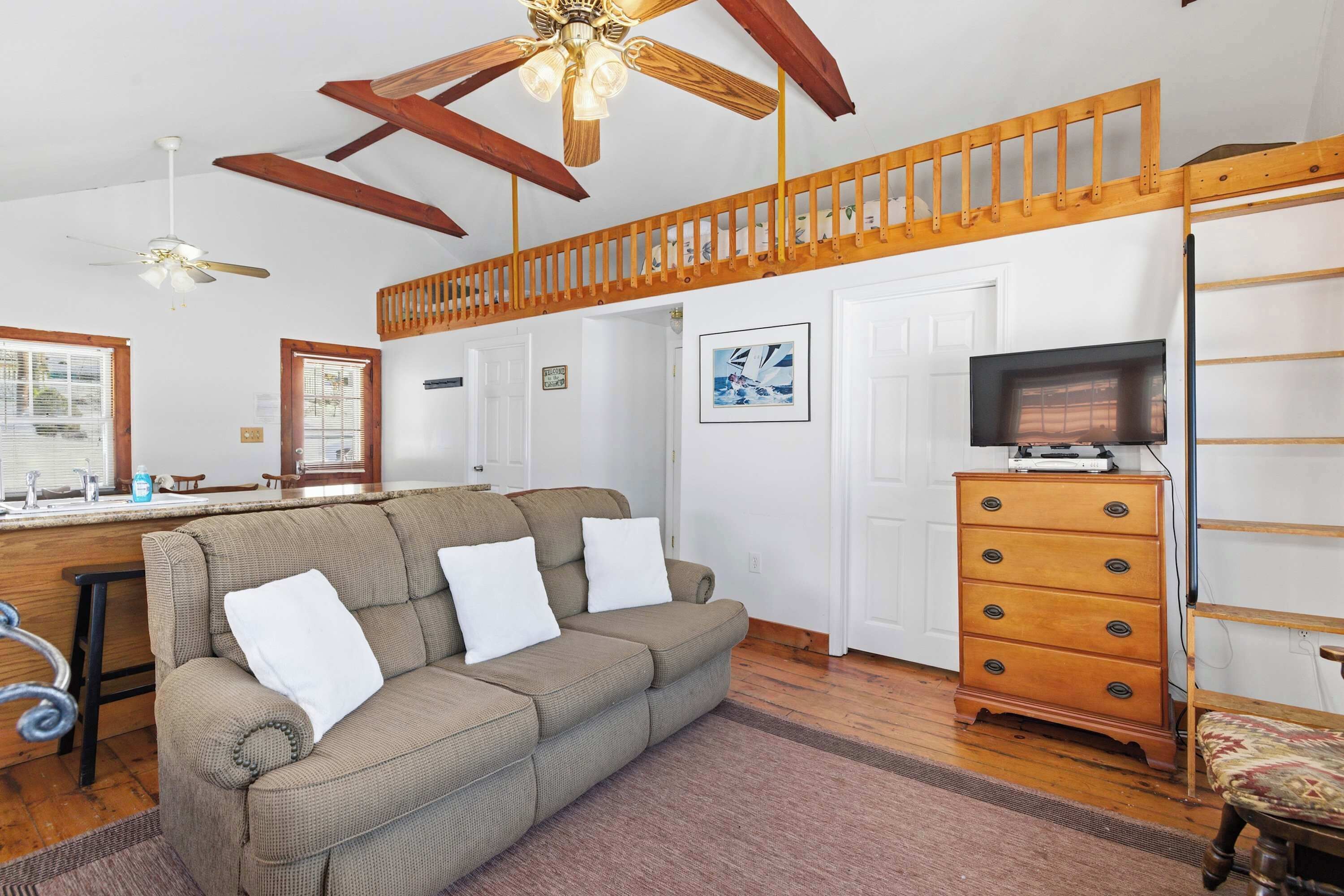 A living room with a sofa, wooden dresser, TV, and a ceiling fan.