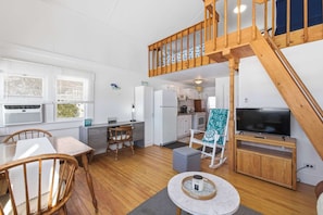 A spacious living area with a wooden staircase, a dining table, chairs, a kitchen area, and a television.