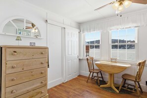 Une pièce avec une commode en bois, une table à manger avec des chaises et une vue dégagée sur l’extérieur grâce à de grandes fenêtres.
