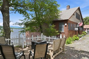 A log cabin with a white picket fence, a table, and two chairs in front.