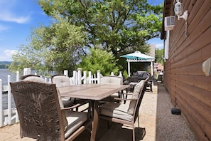 Una terraza de madera con una mesa y sillas, una valla blanca y vistas al lago.