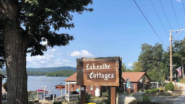 A wooden sign for Lakeside Cottages with a view of a lake and cabins.