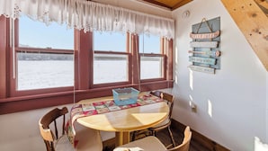 A cozy dining area with a round table, chairs, and a view of a snowy landscape through large windows.