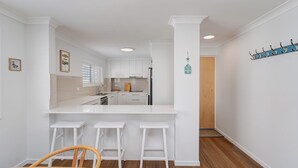 Uma cozinha moderna com armários brancos, uma ilha central com banquetas e uma porta de madeira que dá para outro espaço.