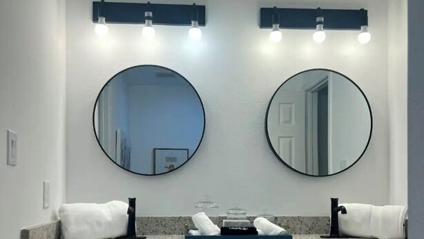 A bathroom with two round mirrors, a countertop with toiletries, and a white door. - Fabulous 4-bedroom 2.5 bath Lake Cottage (Montgomery)