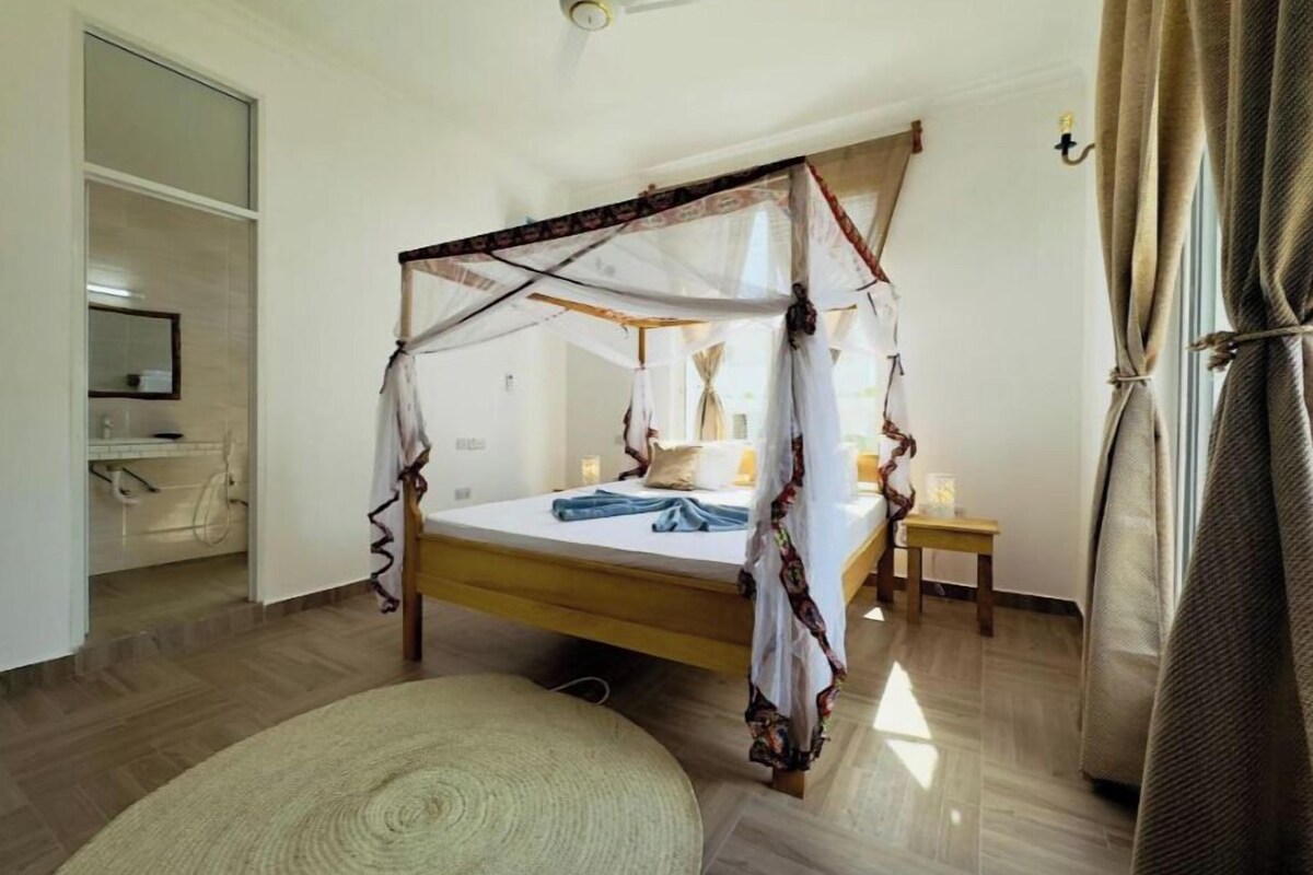 A bedroom with a canopy bed, a bedside table, a small rug, and a ceiling fan.