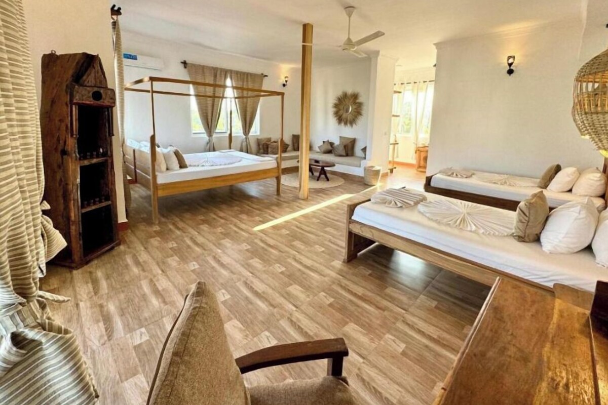 A spacious bedroom with a large bed, a smaller sofa, a wooden bookshelf, and a ceiling fan.