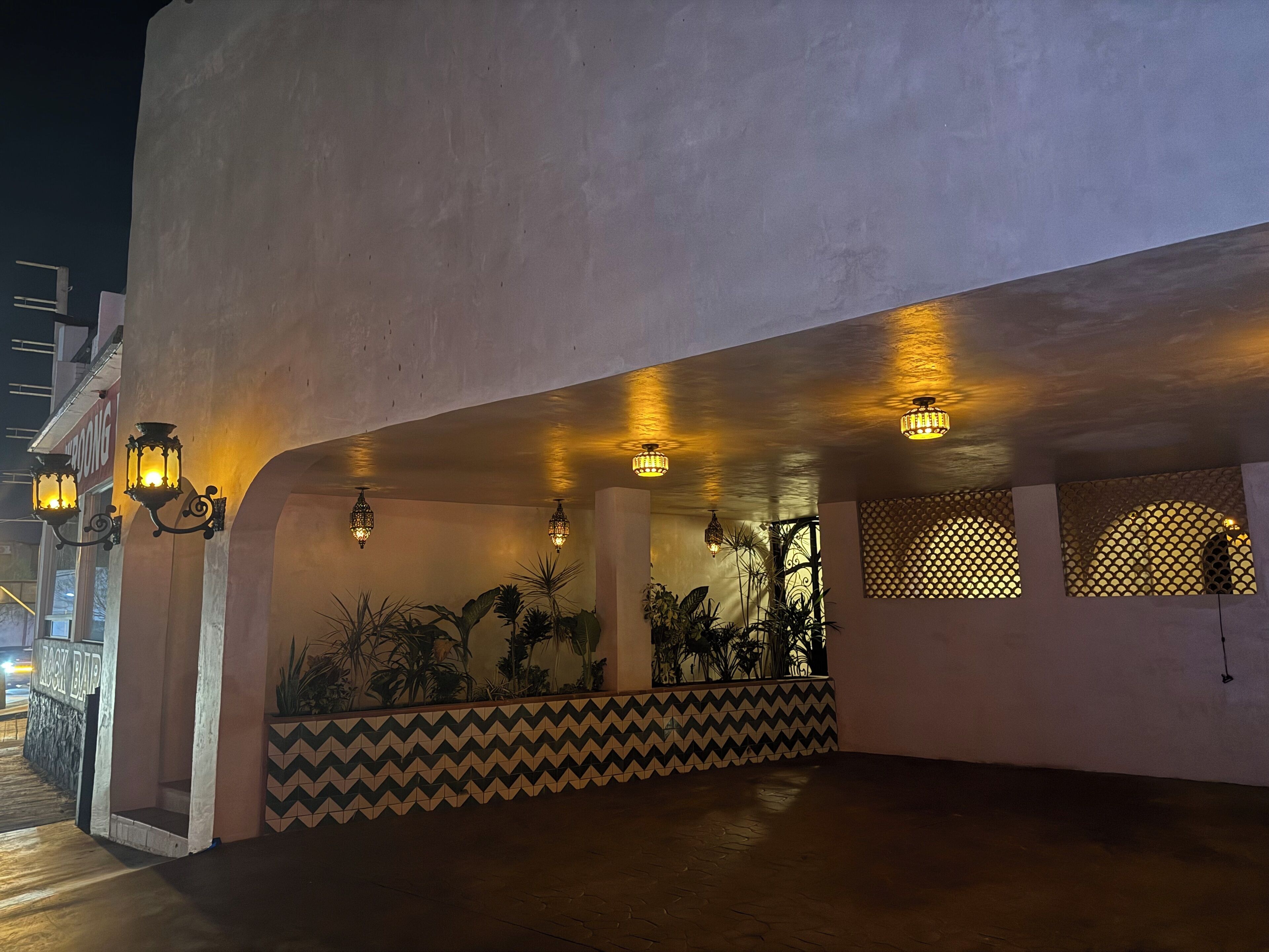 A building with a covered outdoor area featuring patterned tile walls, potted plants, and decorative lighting.