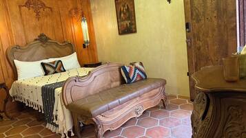 Un dormitorio con cabecera de madera, cama con almohadas estampadas, una banca y una puerta con un número.
