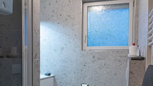 A bathroom with a shower, toilet, and a window. - Apartmenthaus am Park Wohnung 1 (Wilhelmshaven)