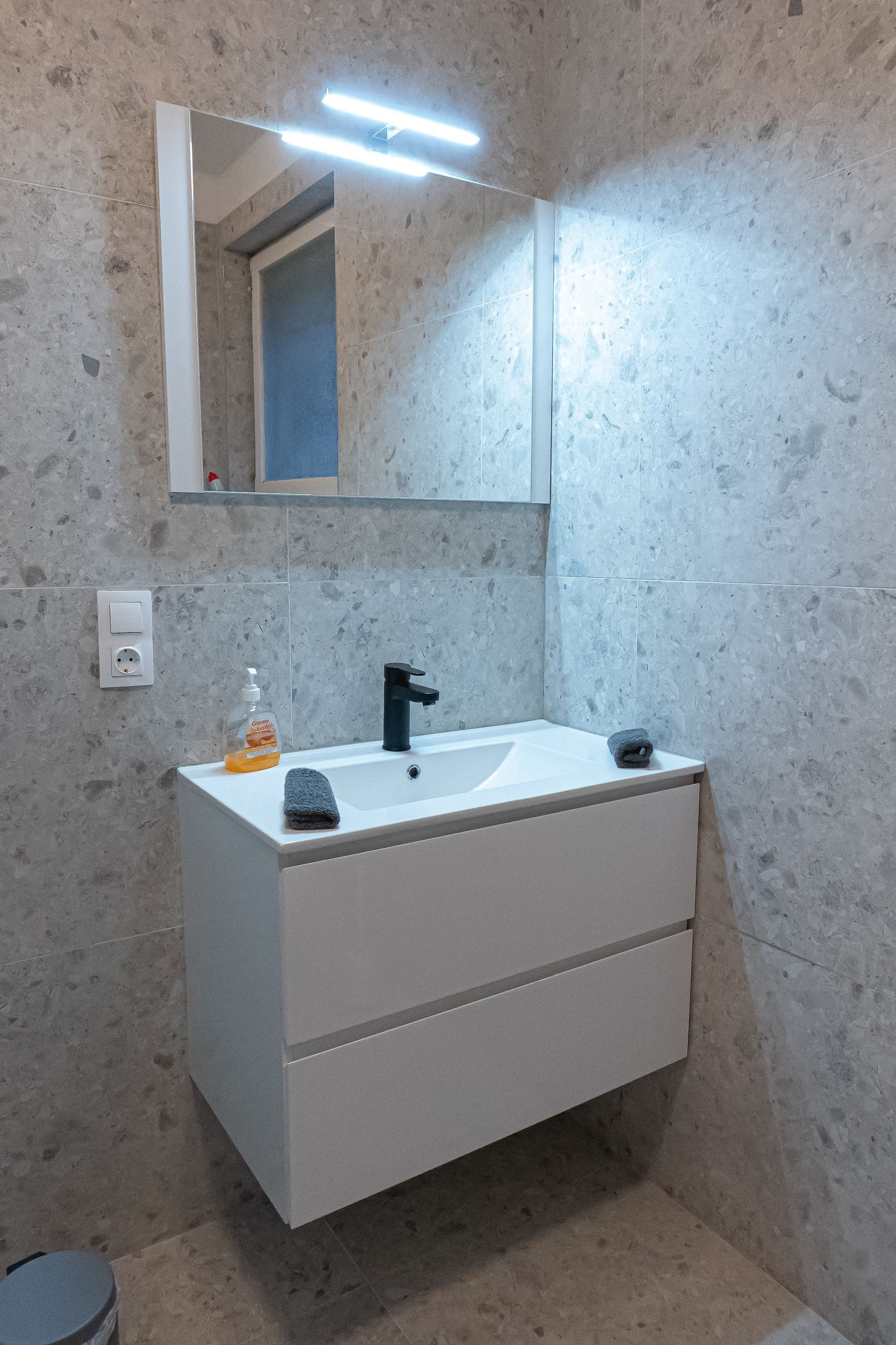 Une salle de bain avec un meuble-lavabo blanc, un robinet noir, un miroir et un distributeur de savon.