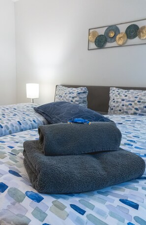 A neatly made bed with a patterned bedspread, a blue pillow, and a folded gray towel. - Apartmenthaus am Park Wohnung 1 (Wilhelmshaven)