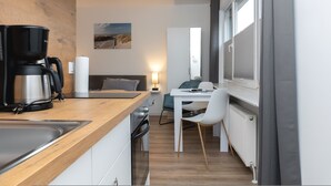 Ett kompakt kök med en kaffebryggare, en matplats med bord och stolar samt utsikt genom ett fönster.