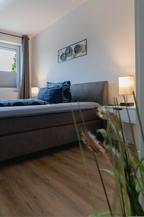 Une chambre à coucher avec un lit, des lampes de chevet, une fenêtre avec des rideaux et une œuvre d’art accrochée au mur.