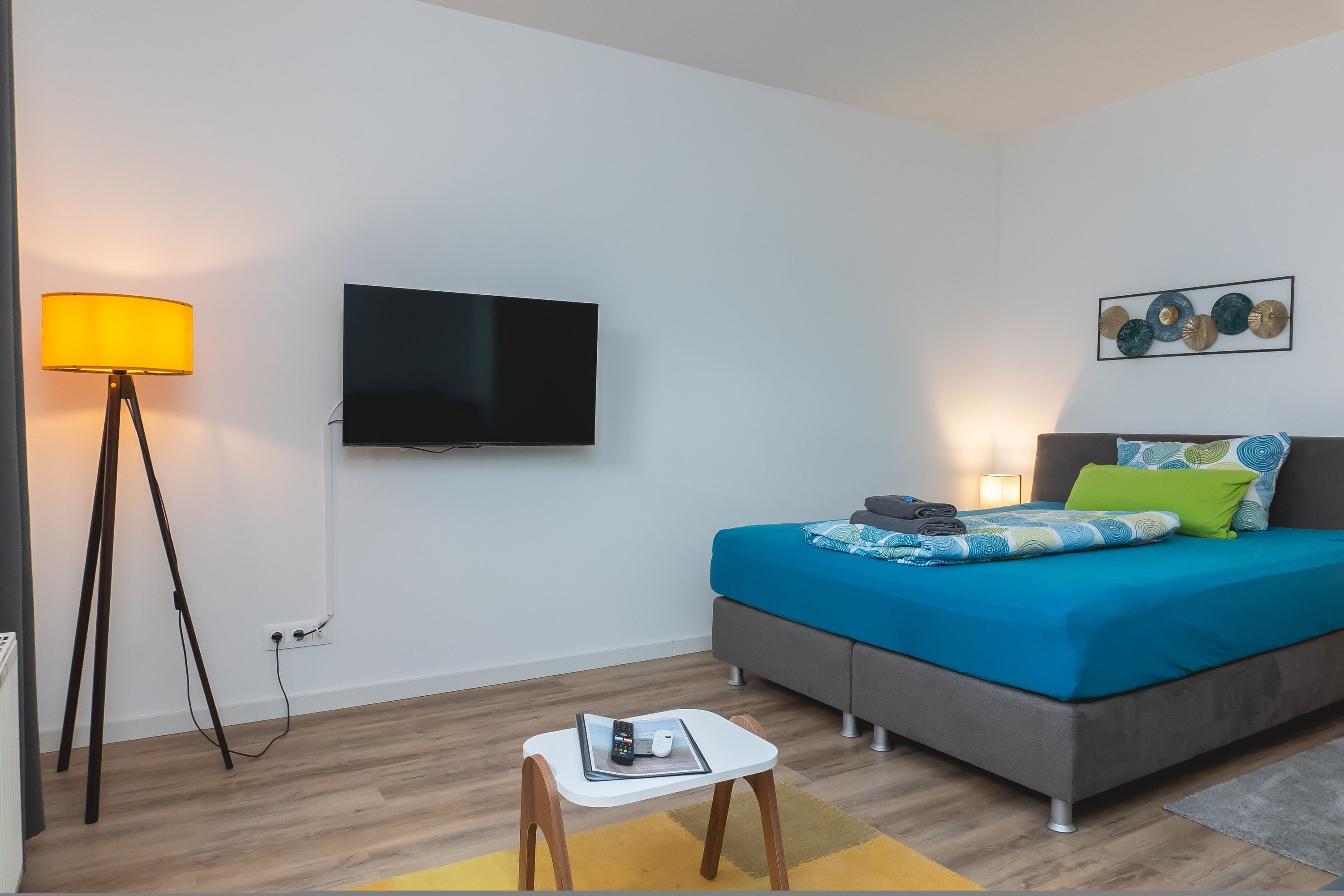 A modern bedroom with a bed, bedside table, lamp, TV, and artwork on the wall.