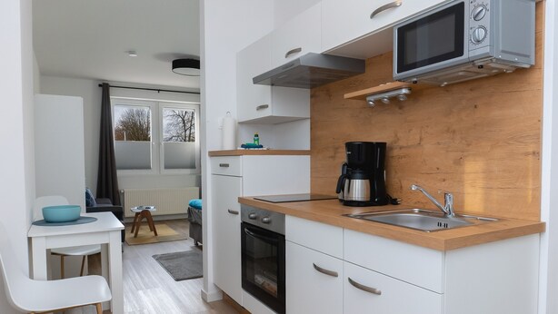 Una cucina compatta con mobili bianchi, un piano di lavoro in legno, un forno a microonde, una macchina da caffè e un lavello.