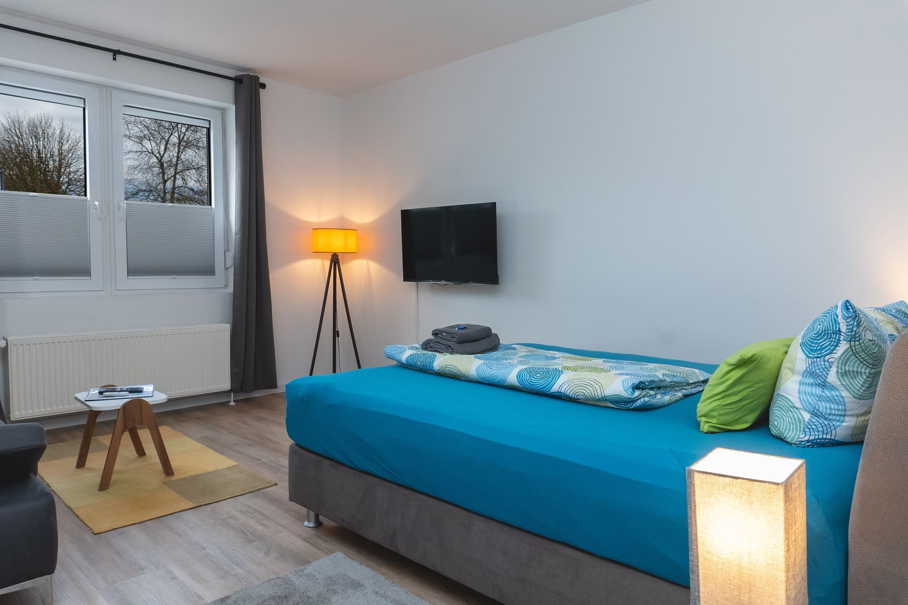A bedroom with a bed, a TV, a lamp, and a window with curtains.
