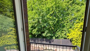 A balcony with a glass door, two chairs, a small table, and a wooden fence. - Apartmenthaus am Park Wohnung 7 (Wilhelmshaven)