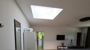 A room with a skylight, a flat-screen TV mounted on the wall, and a door leading to an outdoor area. - Apartmenthaus am Park Wohnung 7 (Wilhelmshaven)