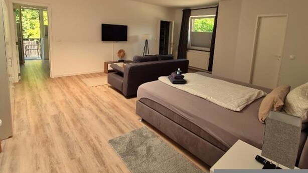 A modern bedroom with a large bed, a sofa, a TV, and a skylight. - Apartmenthaus am Park Wohnung 7 (Wilhelmshaven)
