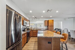 Una cocina moderna con electrodomésticos de acero inoxidable, armarios de madera, encimeras de granito y una isla central con asientos.