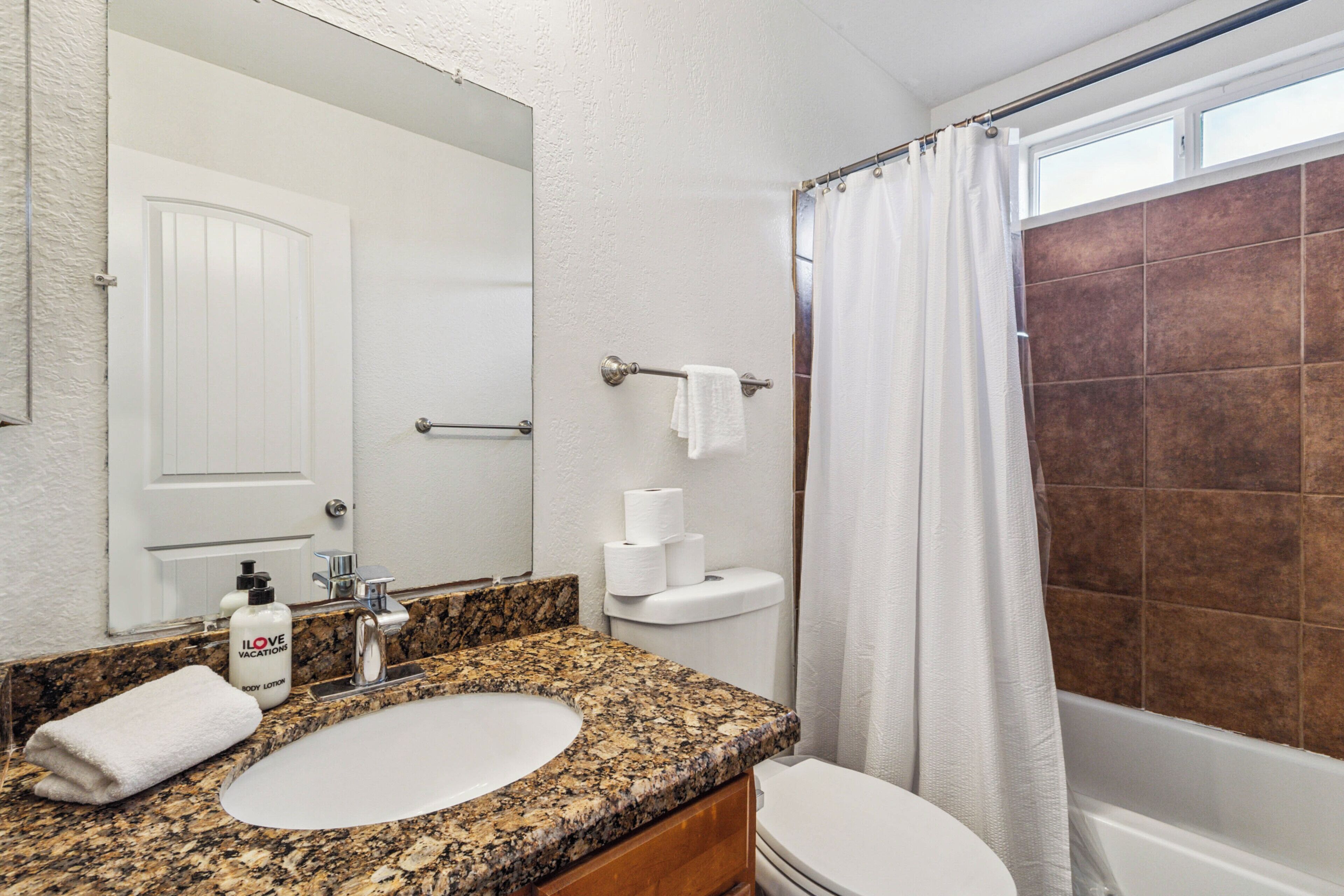 Une salle de bain avec un lavabo à vasque en granit, des toilettes blanches, une douche avec un rideau et un miroir au-dessus du lavabo.