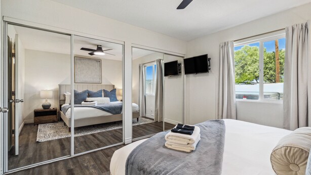 Ein Schlafzimmer mit Bett, Deckenventilator, Fernseher und einem Fenster mit Vorhängen.