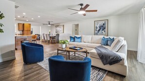 Ein modernes Wohnzimmer mit einer Couch, blauen Sesseln, einem Couchtisch und einem Deckenventilator.