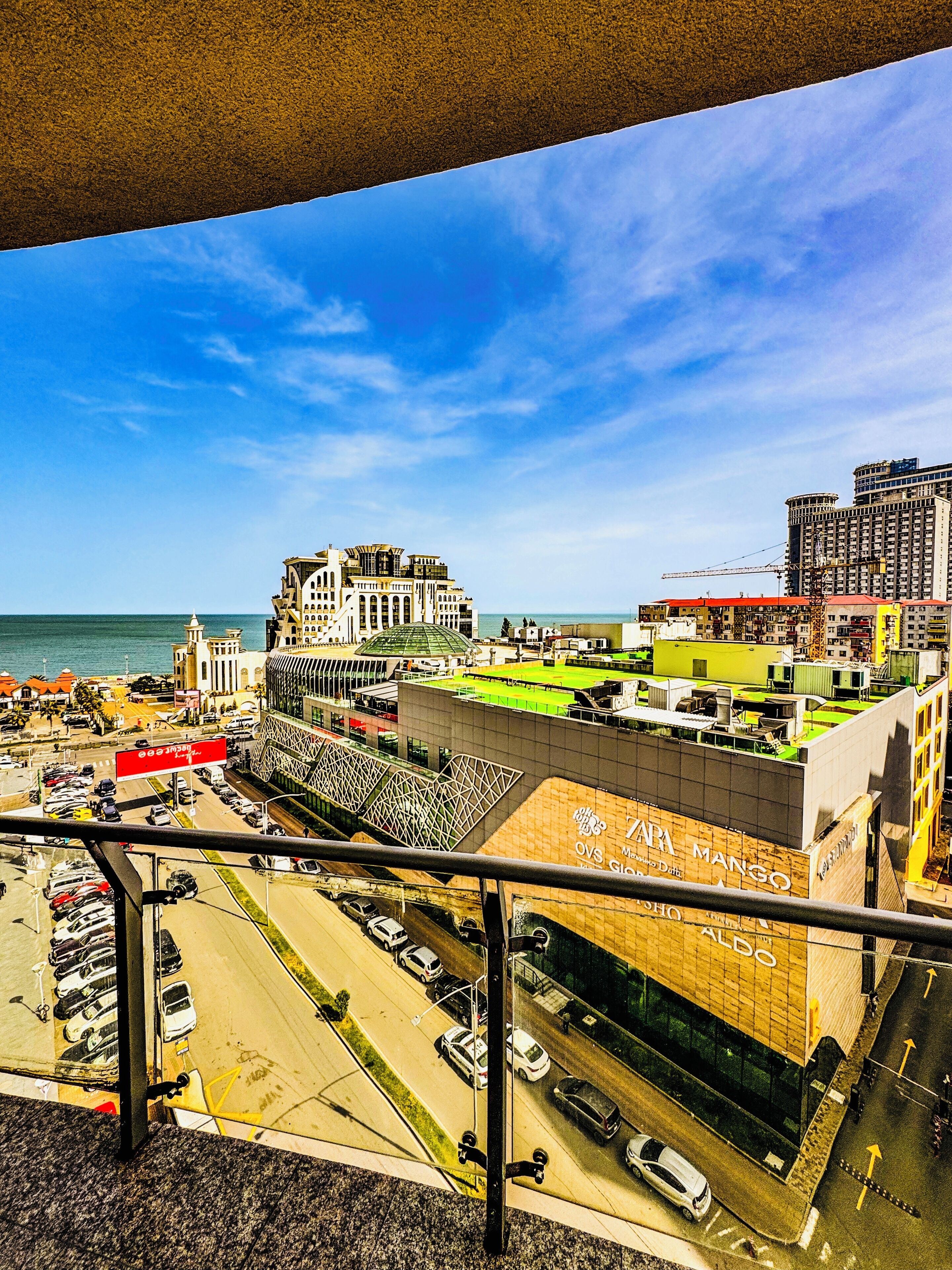 Une vue sur la ville avec la mer en arrière-plan, un grand bâtiment doté d’un toit végétalisé et un parking rempli de voitures.