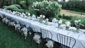 A long table set outdoors with white tablecloths, black chairs, and floral centerpieces.