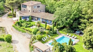 A large two-story house with a swimming pool, surrounded by well-maintained gardens and a stone pathway.