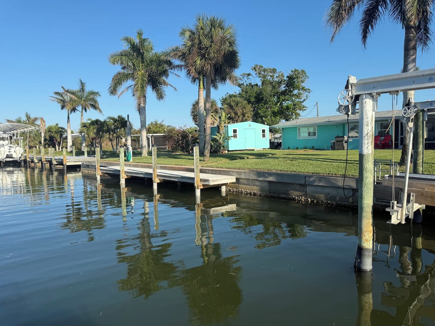 Un puerto deportivo con barcos amarrados, una pequeña casa azul y palmeras.