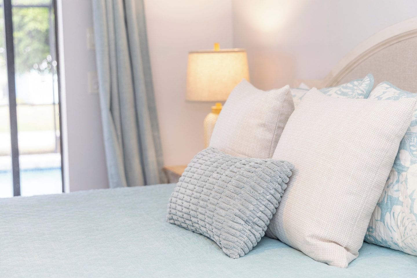 A bed with a light blue bedspread and two pillows, one with a textured pattern and the other plain.