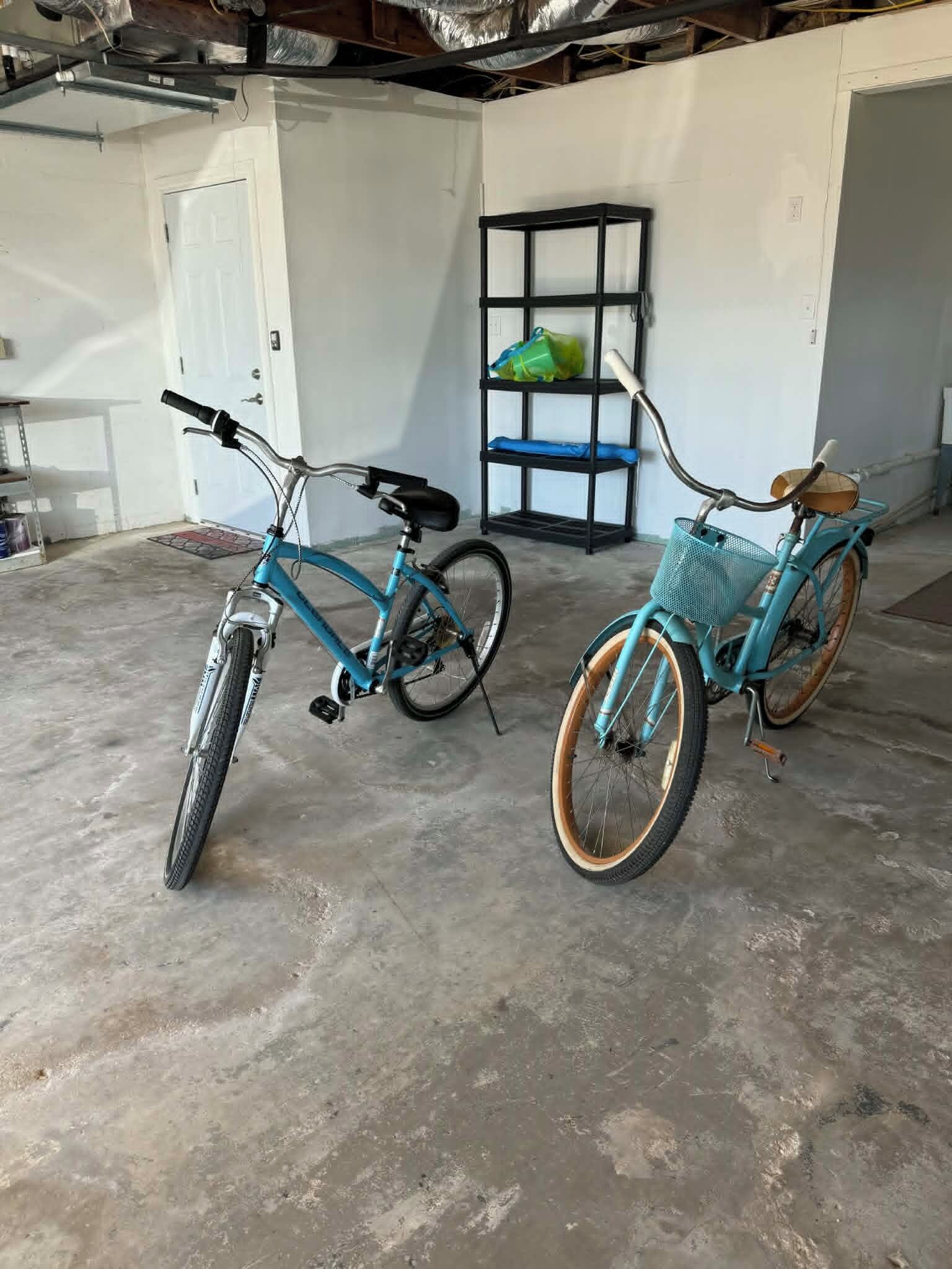 Due biciclette parcheggiate in un garage con uno scaffale metallico e una porta sullo sfondo.