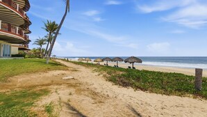 Una spiaggia con un albergo, palme e ombrelloni di paglia.
