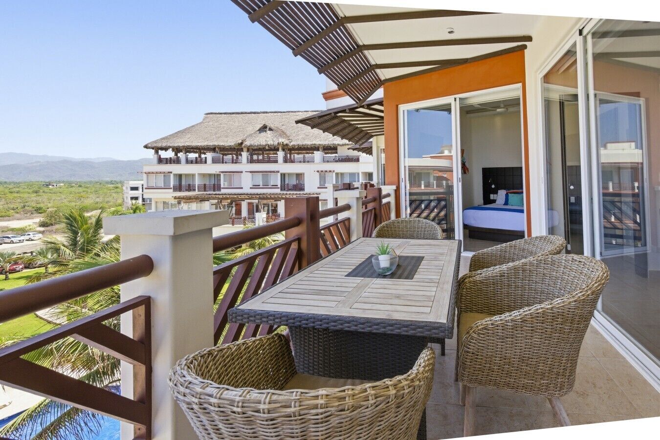 Ein Balkon mit Korbmöbeln, einem Tisch und Blick auf ein Hotelgebäude.