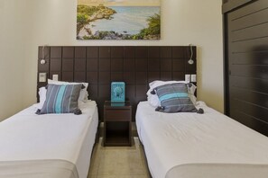 Une chambre d’hôtel avec deux lits, une table de chevet agrémentée d’un objet décoratif et un tableau représentant un paysage côtier.