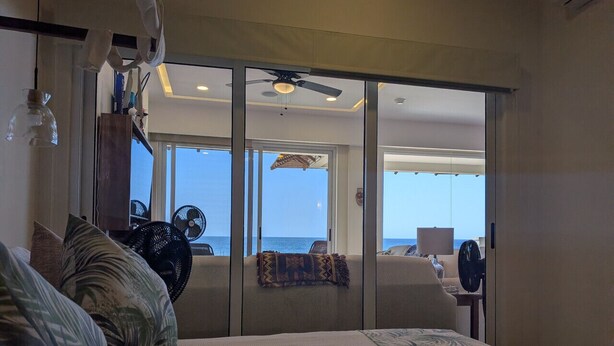 Ein Hotelzimmer mit Bett, Deckenventilator, Meerblick und einer Schiebetür zum Balkon.