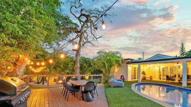 Ein Garten mit Grill, Esstisch, Stühlen, einem Swimmingpool und einem Haus mit großen Fenstern.