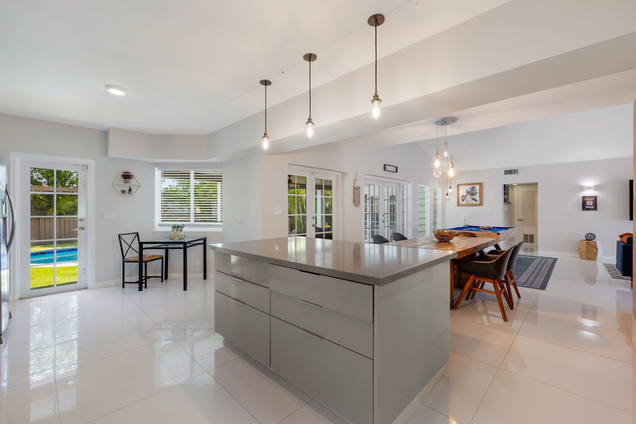 A modern kitchen with a central island, pendant lighting, and a dining area with chairs.