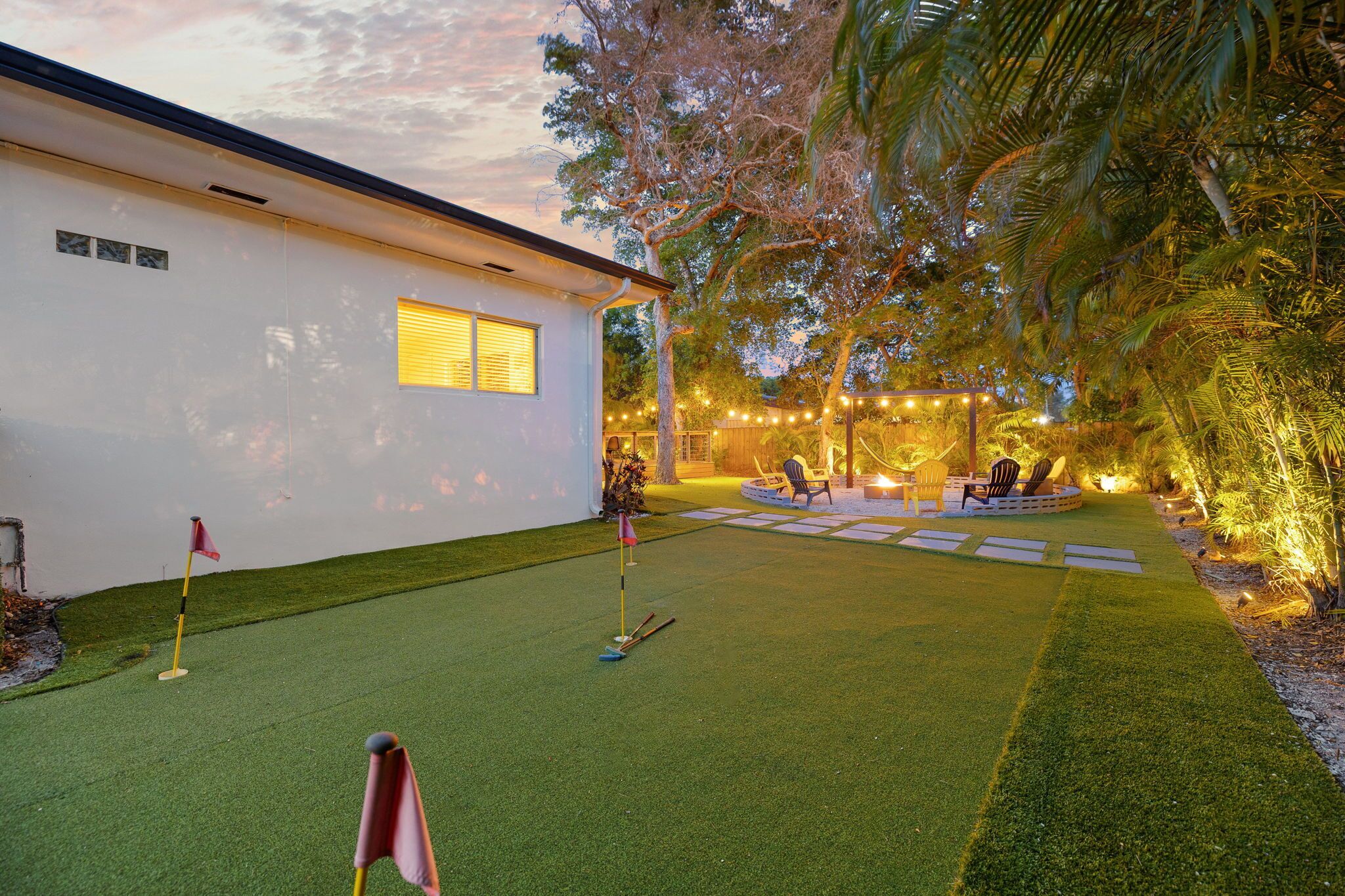 A well-maintained lawn with a putting green, a small building with a window, and string lights in the background.