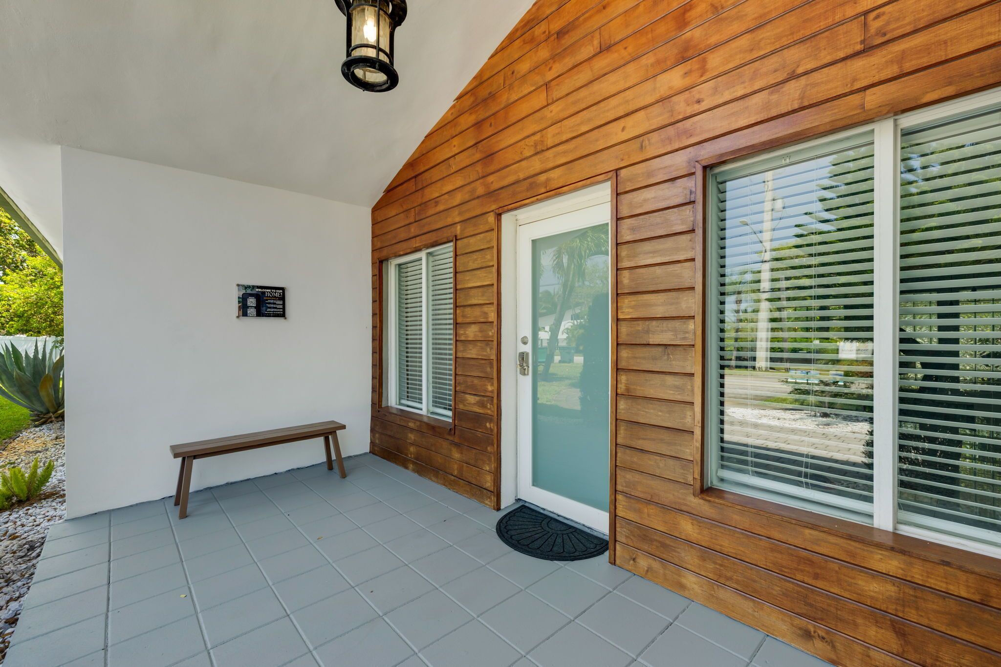 A wooden exterior with a bench, a door, and a window with blinds.