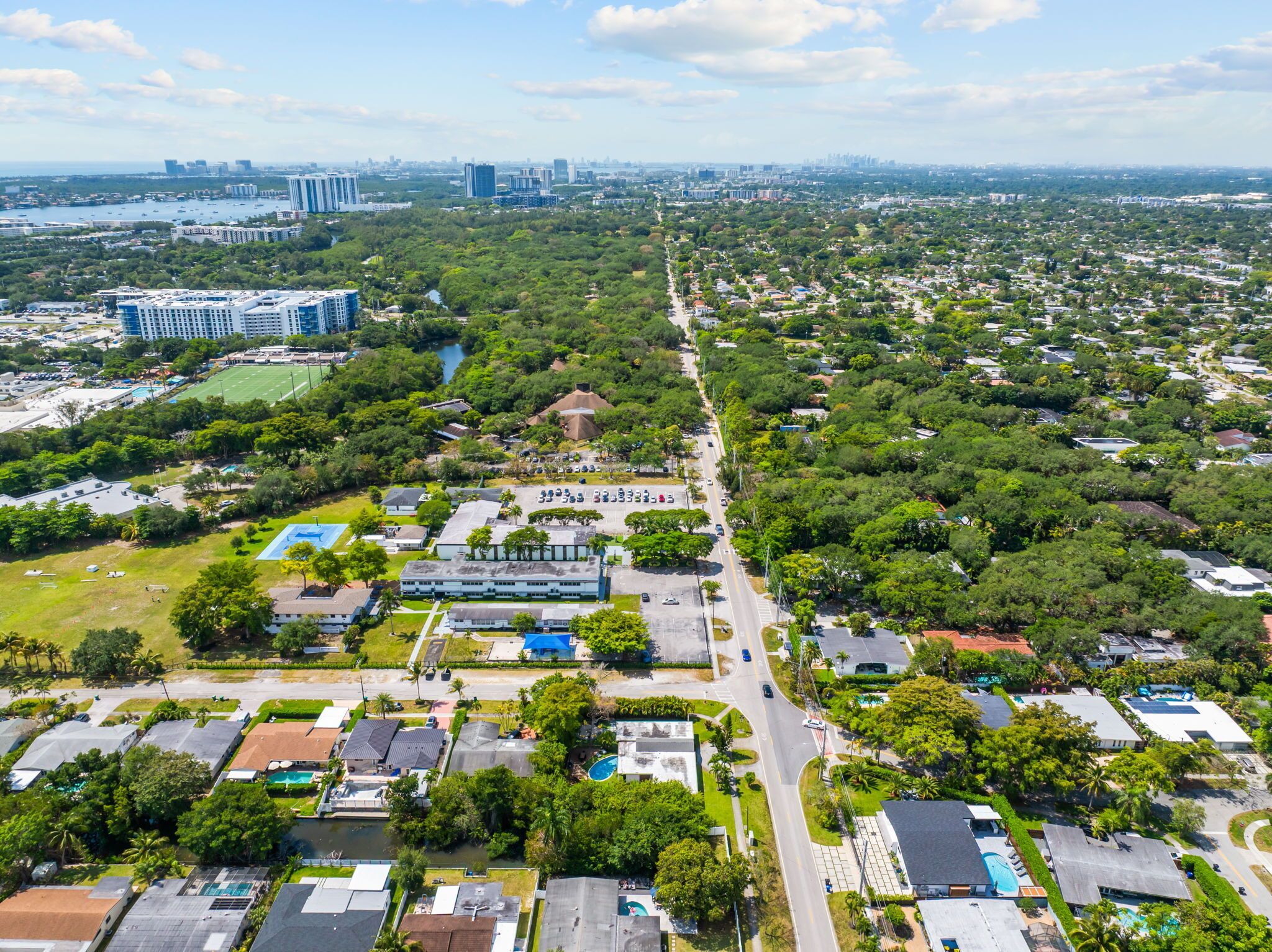 An aerial view of a residential area with a mix of single-family homes and apartment buildings, a main road, and a body of water in the background.