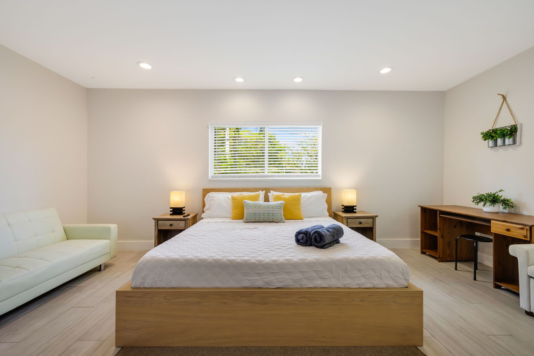 A bedroom with a bed, bedside tables, a desk, a chair, and a window with blinds.