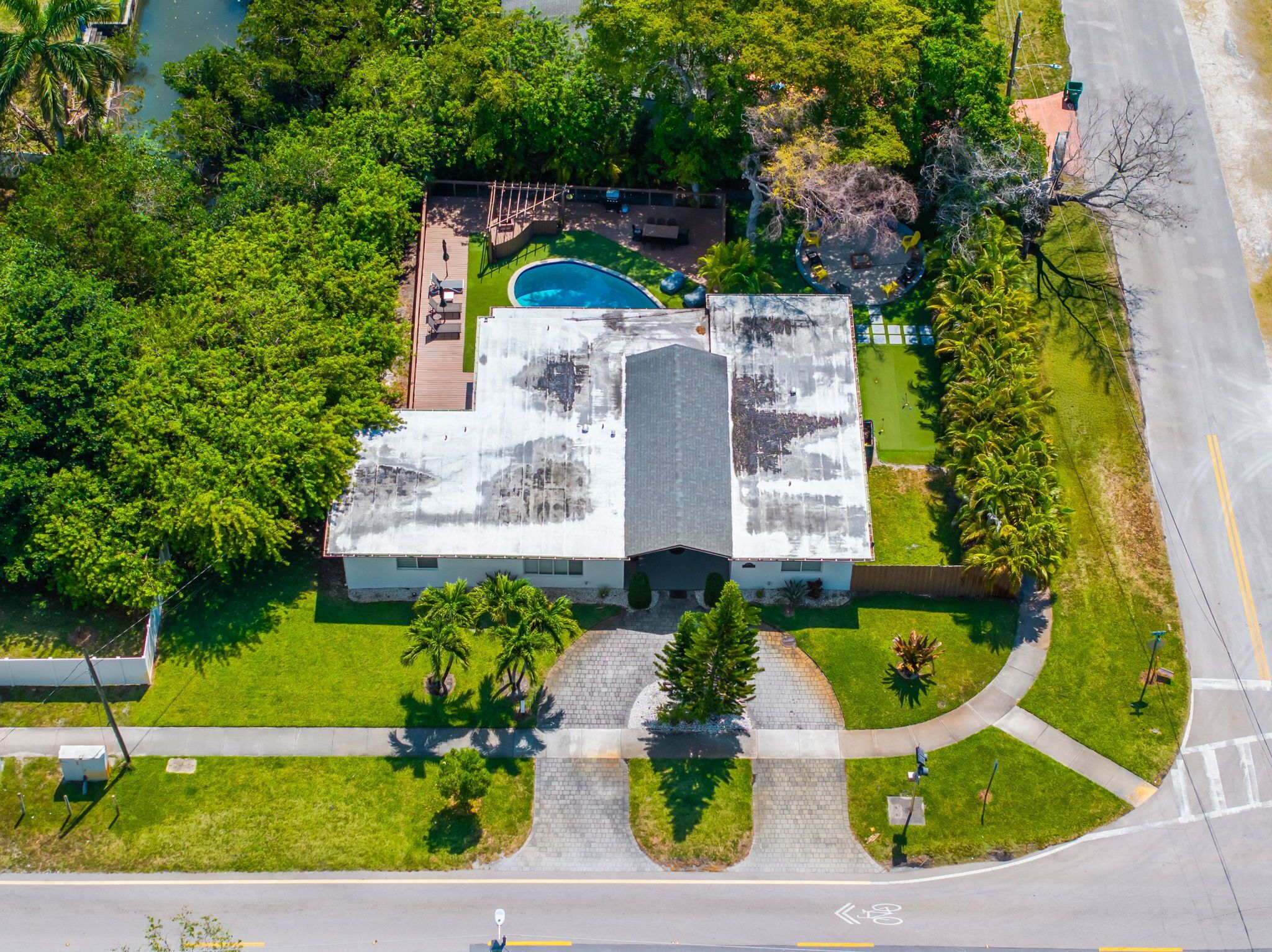 An aerial view of a building with a swimming pool, surrounded by greenery and a paved driveway.